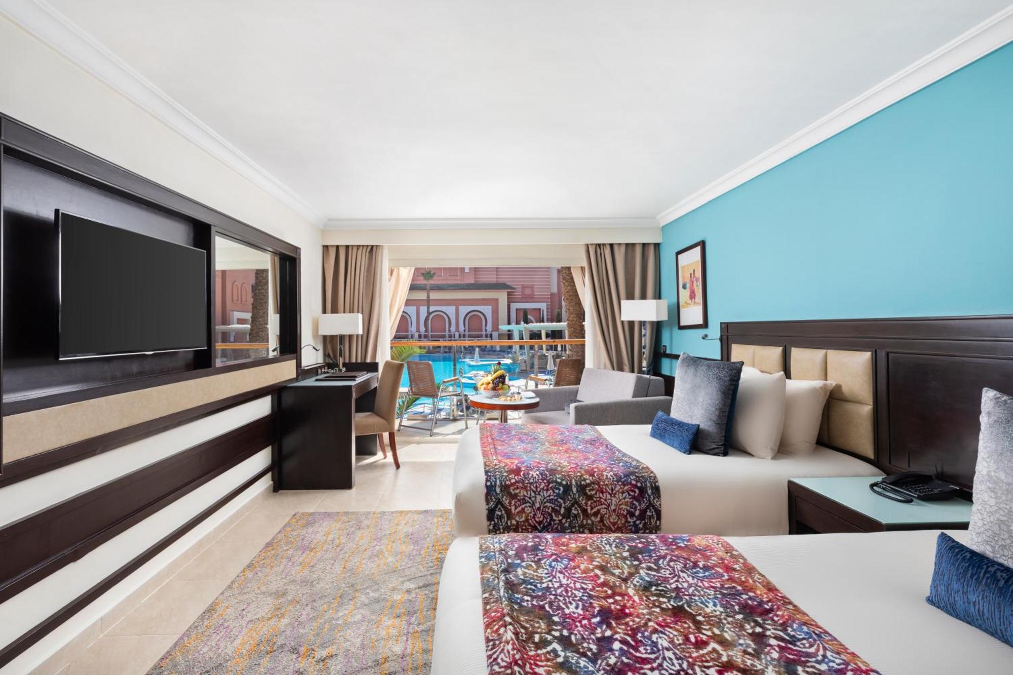 Savoy Le Grand Hotel Marrakech Marrakesh Exterior foto The photo shows a stylish hotel room featuring two beds, each adorned with colorful patterned bedspreads. The walls are painted in a calming blue hue, and there are large windows allowing natural light to fill the space, with a view of an outdoor poo